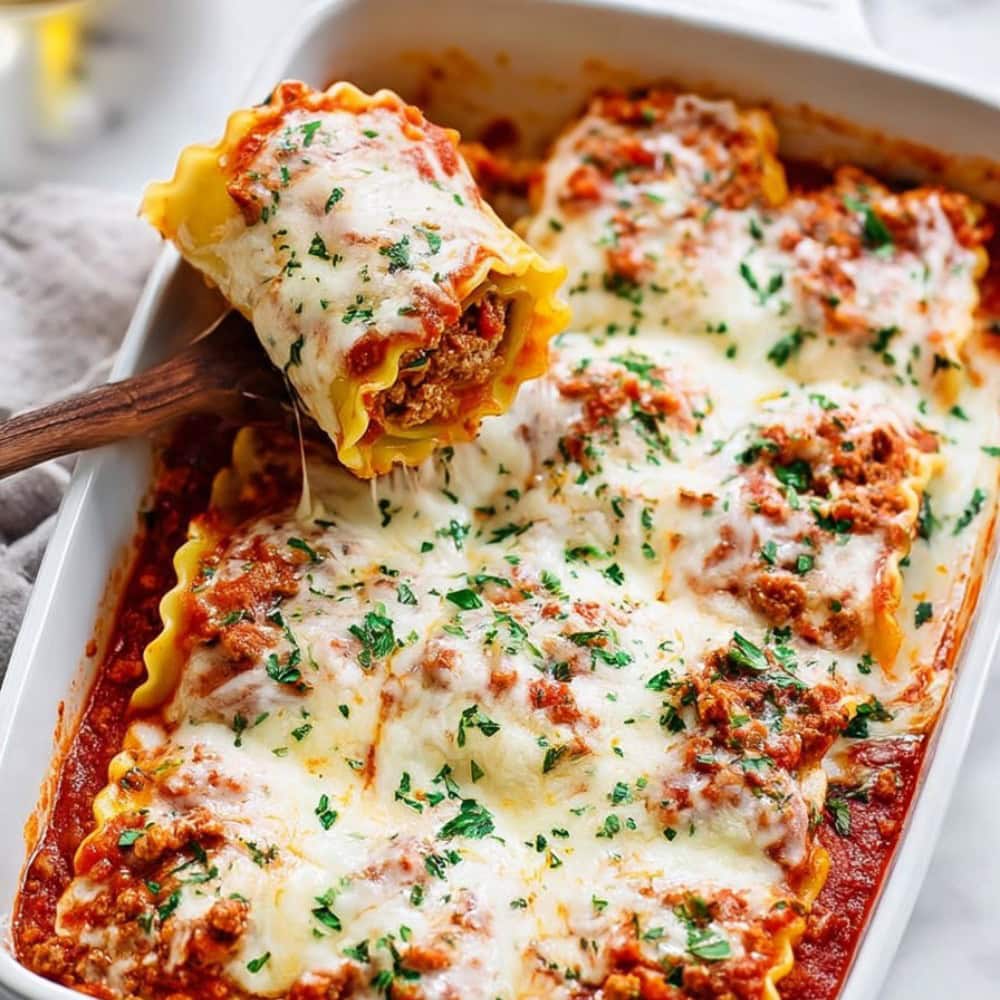 A wooden spoon lifting a lasagna roll up from a baking dish.