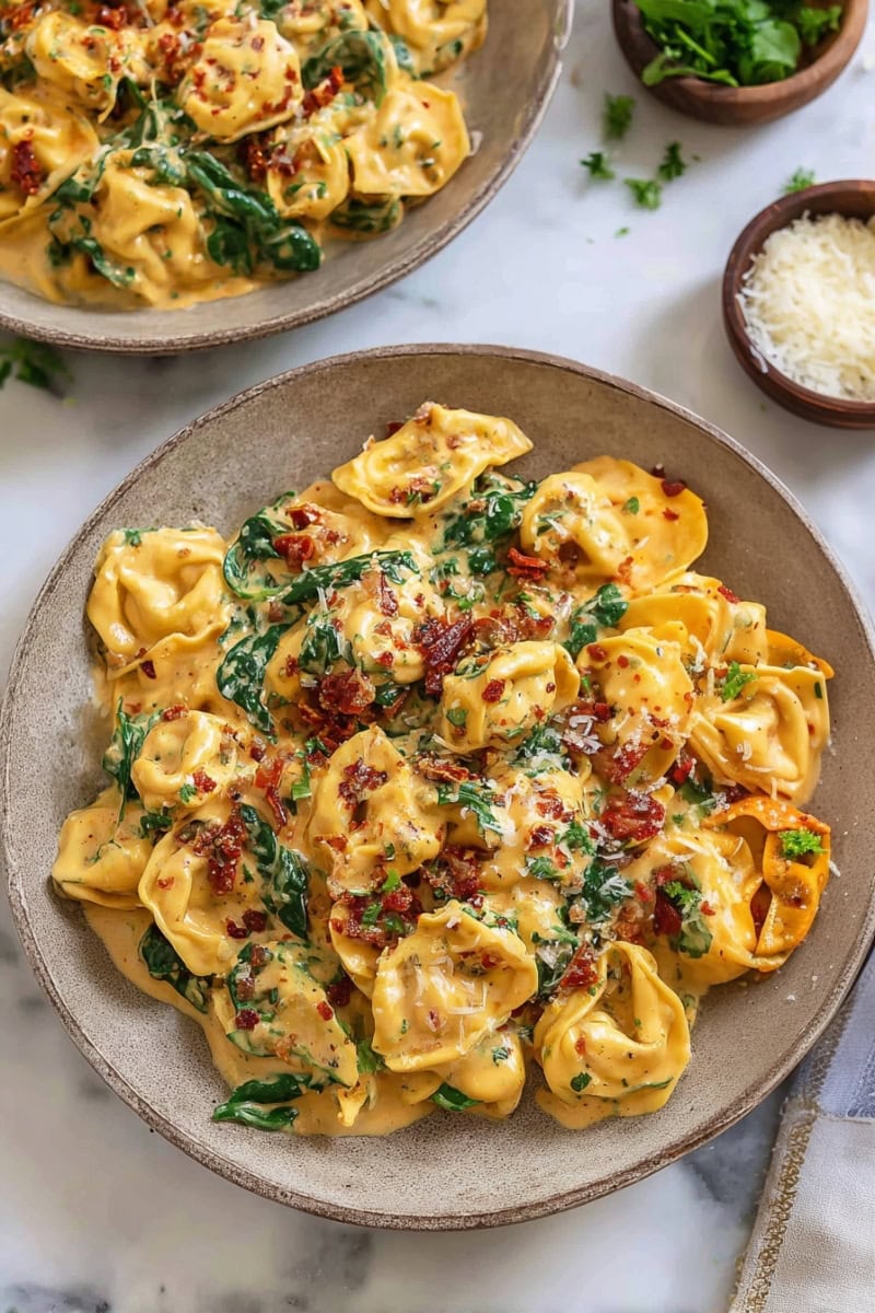 Two bowls of Marry Me Tortellini, loaded with sun-dried tomatoes, spinach, and a sprinkle of Parmesan.