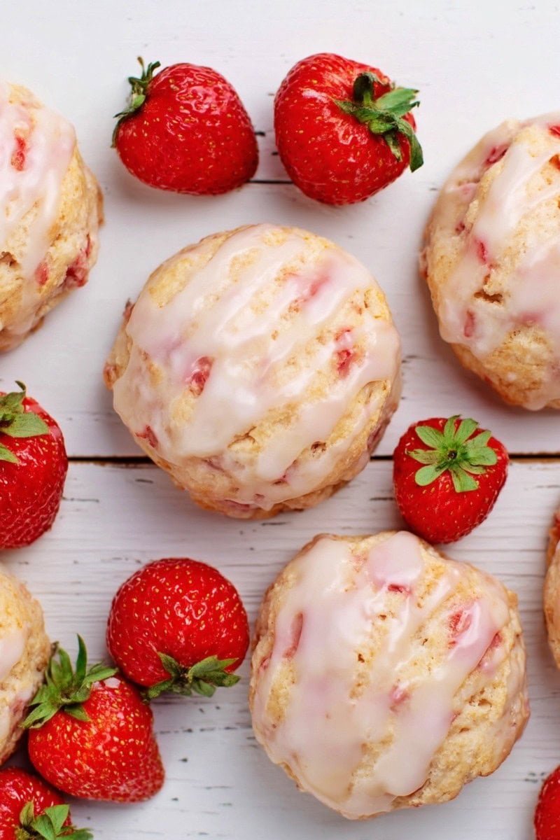 Glazed strawberry biscuits  on a table, surrounded by fresh strawberries.